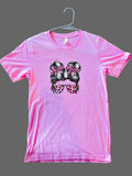 Pink t-shirt with graphic design of hair buns and sunglasses on a beige carpet.